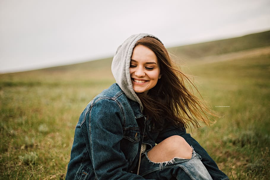 panning photography of female wearing blue denim hoodie while sitting on green grass field, HD wallpaper