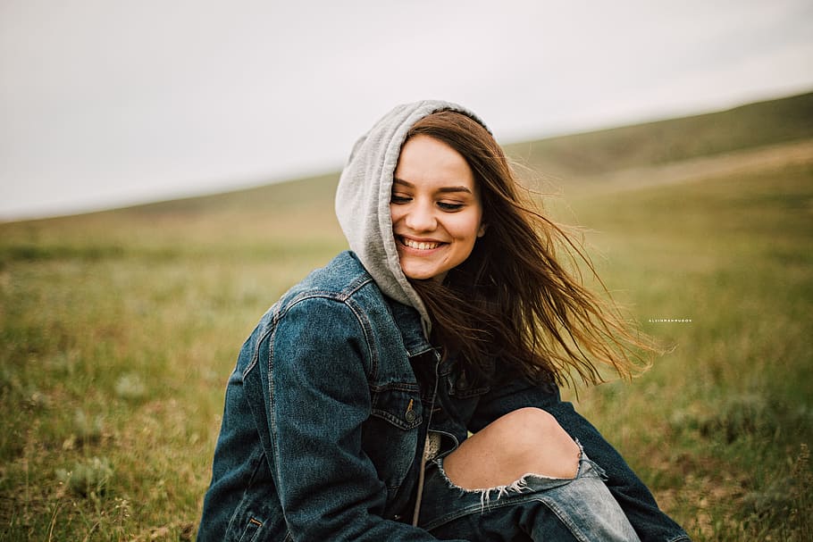 panning photography of female wearing blue denim hoodie while sitting on green grass field HD wallpaper