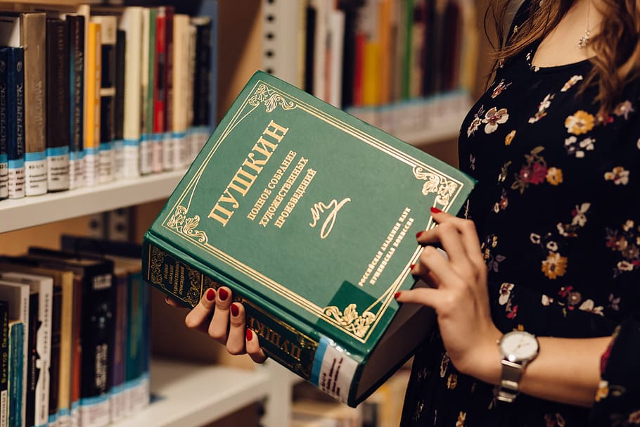 woman holding and opening book in front of book lot on shelves HD wallpaper