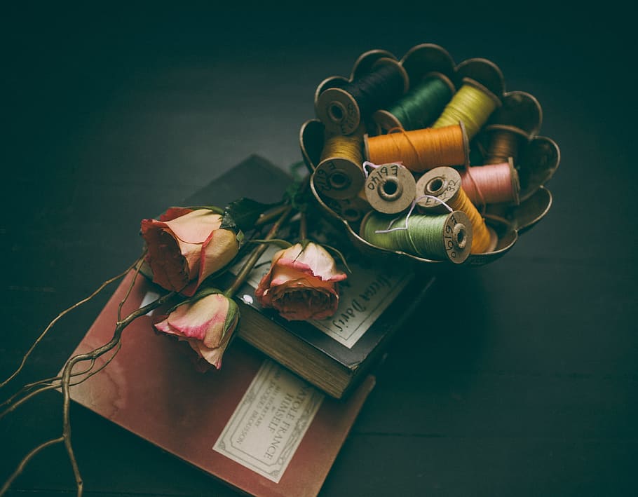 assorted-color thread in bowl beside three roses on two hardbound books, assorted-color sewing threads on brass bowl HD wallpaper