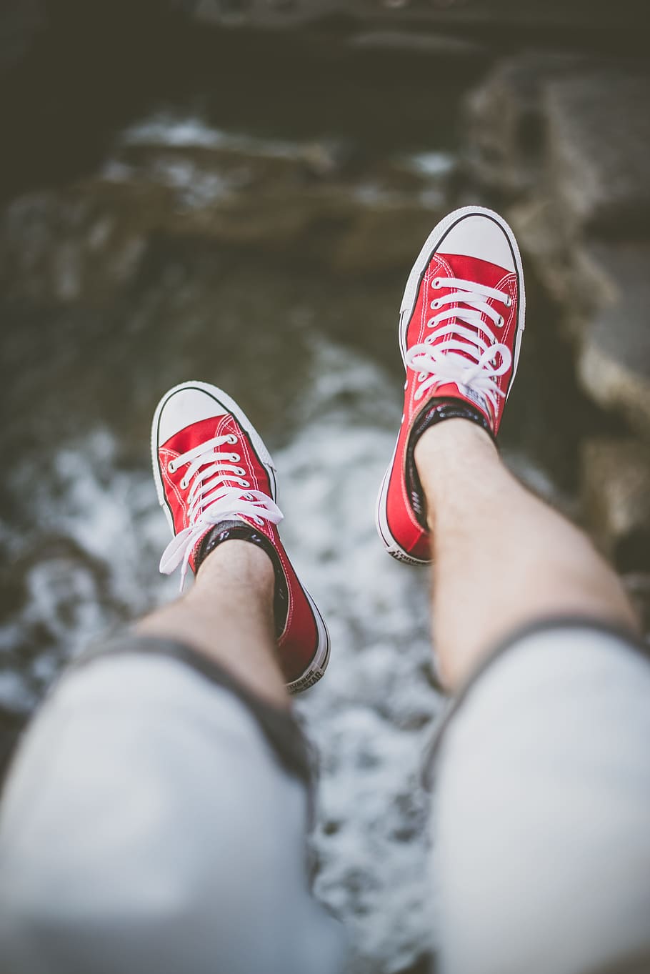 selective focus photography of person wearing red low-top sneakers over body of water, selective focus photography of man's feet wearing red lace-up low-top sneakers above body of water