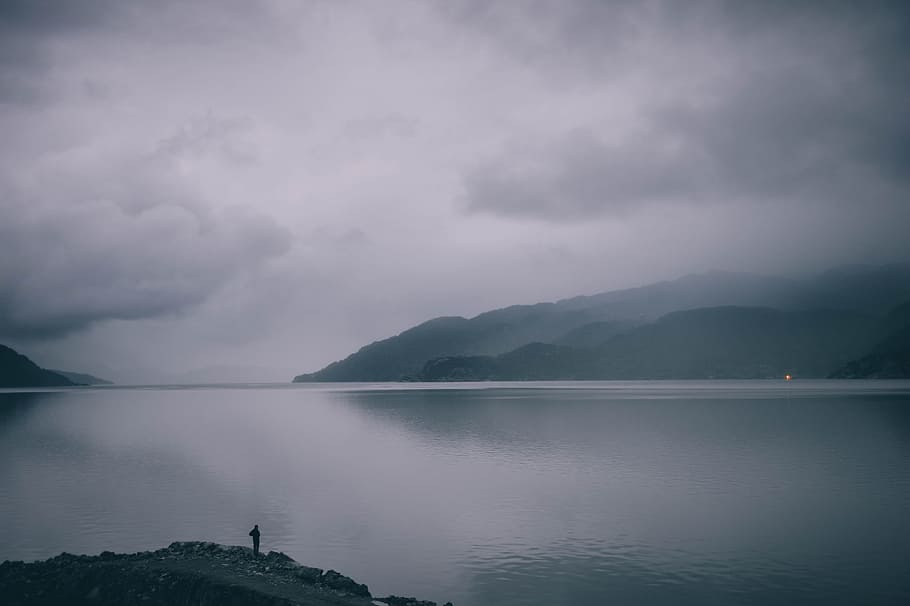 man standing on gray mountain, silhouette of mountain near body of water during foggy day HD wallpaper