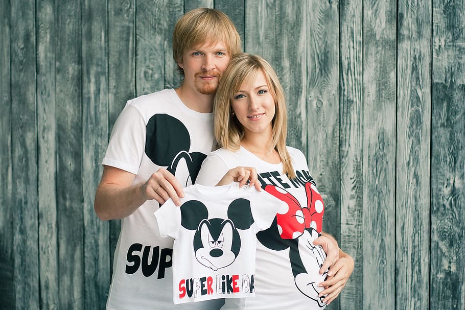 man and woman holding Mickey Mouse shirt, pregnancy, baby's bootees