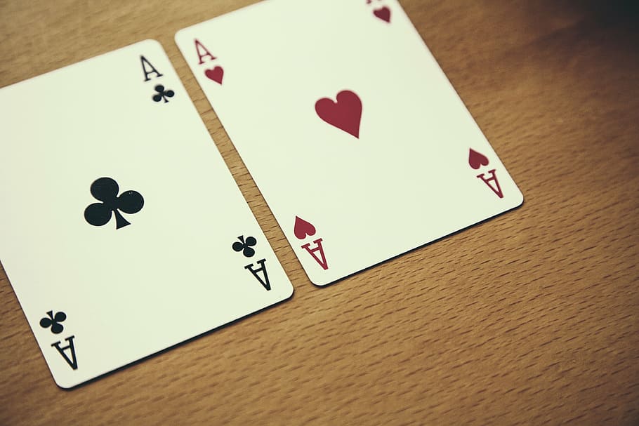 selective focus photography of two aces of hearts and clove playing cards on brown surface