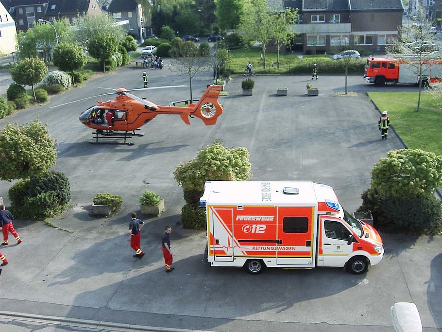 white and orange vehicle near people and helicopter, ambulance