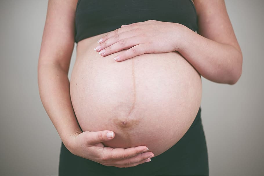 closeup photography of pregnant woman holding her stomach wearing black crop top and black bottoms