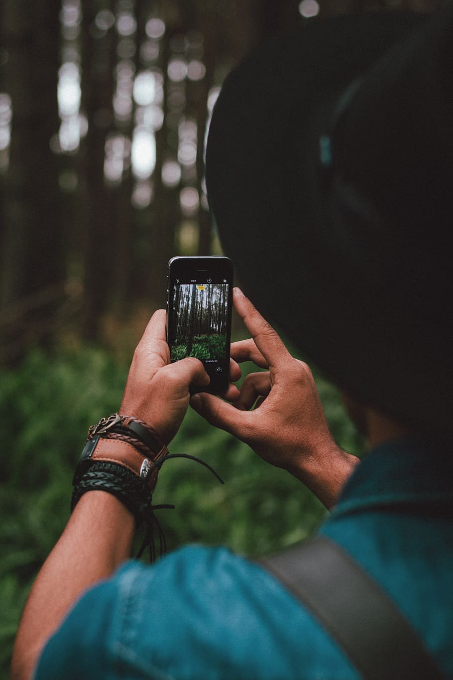 man holding iPhone 5s, person in blue shirt and black hat holding black smartphone HD wallpaper