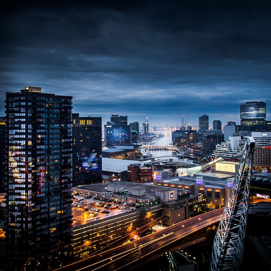 aerial photography of body of water surrounded by lighted buildings and roads under dramatic clouds, aerial view of city during night HD wallpaper