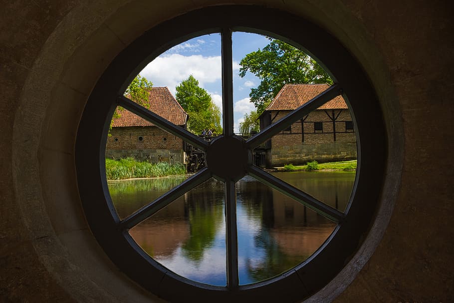 photo of lake near houses taken through round black framed clear glass window HD wallpaper