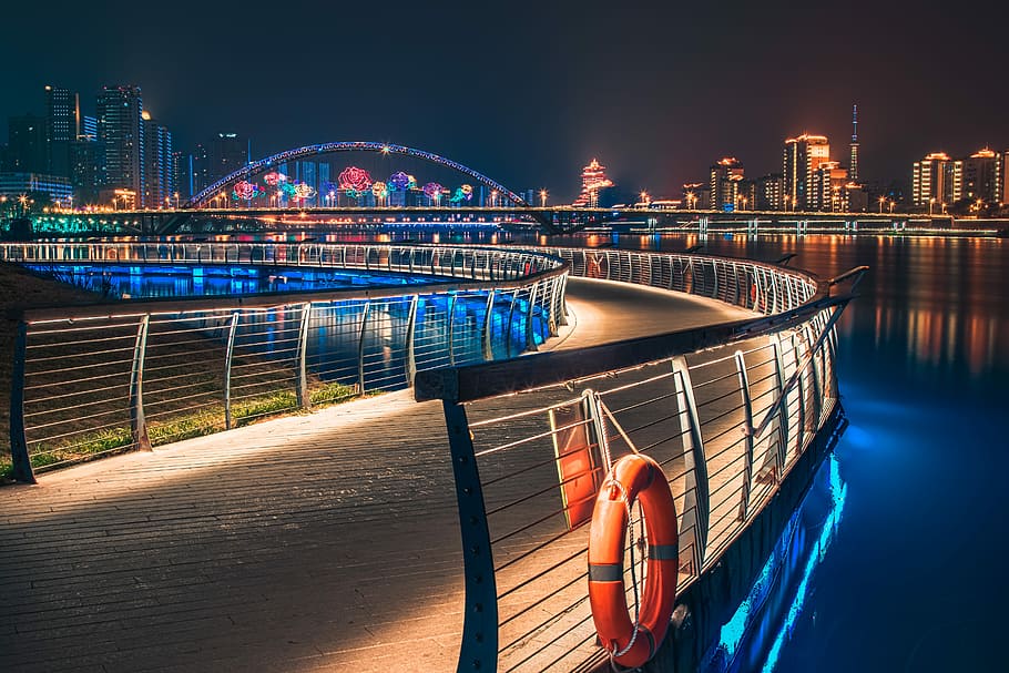 curve road with railings near buildings with lights at night, pathway between railings HD wallpaper