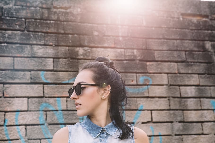 photography of woman in faded blue denim collared vest wearing black sunglasses near gray wall, woman standing near brick wall, HD wallpaper