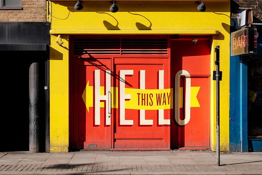 photo of orange Hello print gate, red metal gate hello this way printed on yellow building at daytime HD wallpaper