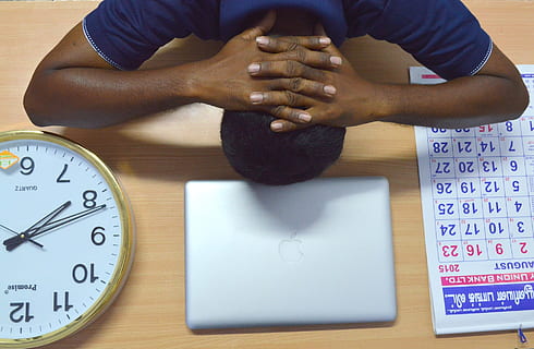 man lying on beige table near silver MacBook and brass-colored analog clock and monthly calendar HD wallpaper