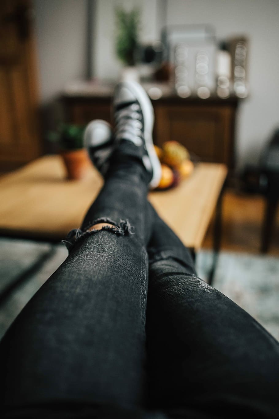 Woman in ripped jeans and black sneakers with a silver laptop on a wooden table HD wallpaper