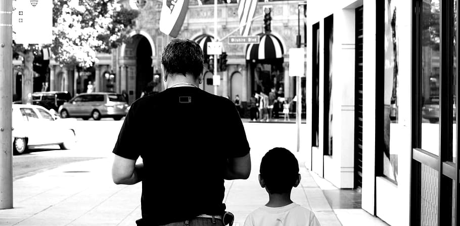 grayscale photo of man and boy walking beside building, father's day