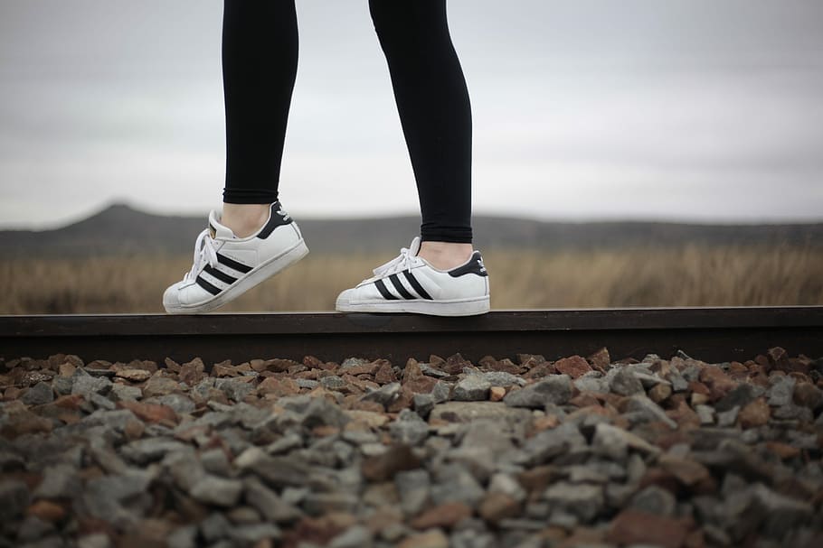 person wearing white-and-black adidas superstar, selective focus photo of woman standing on train rail