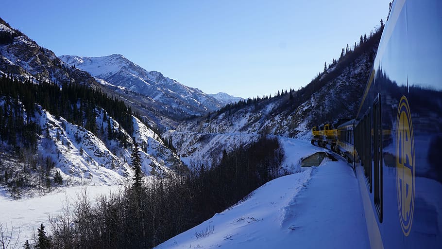 blue and yellow locomotive travelling through mountains covered with snow, photograph of train passing beside mountain ranges, HD wallpaper