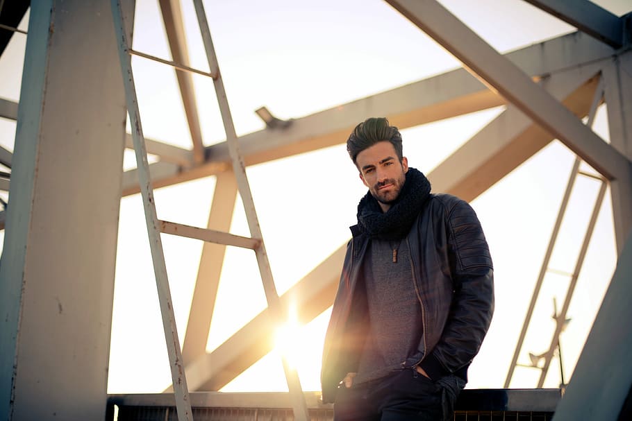 man wearing jacket and put his two hands in pocket, man standing beside white metal frame HD wallpaper