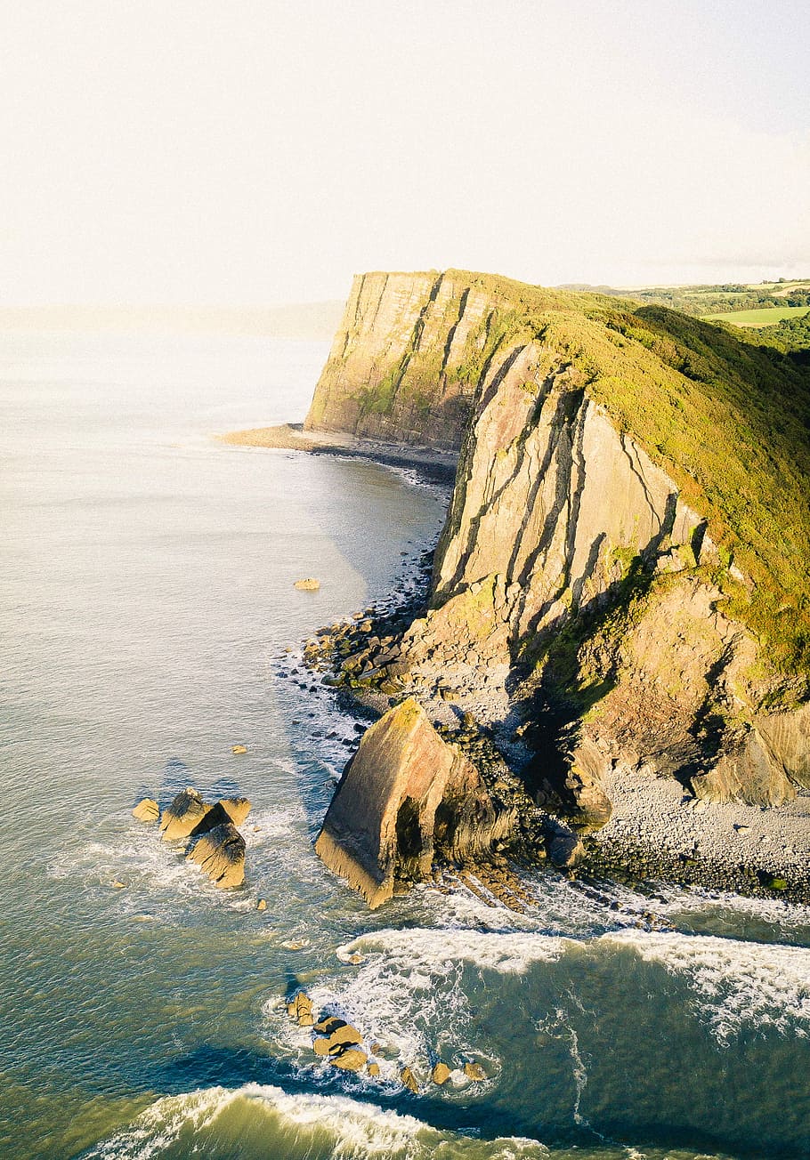 aerial shot of cliff near body of water, gray mountain surrounded ocean water under gray sky HD wallpaper