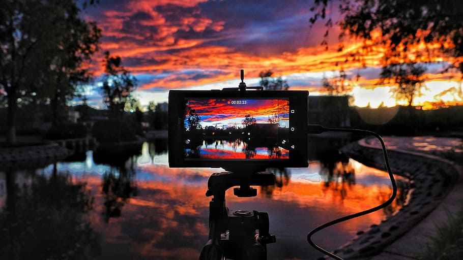 golden hour photography of body of water surrounded of trees, camera on tripod taking picture of lake during sunset HD wallpaper