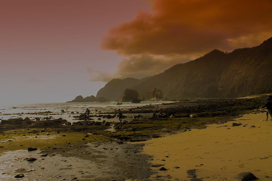 black mountain near sea under white sky during golden hour, dim clouds approaching above rocky seashore near mountain HD wallpaper