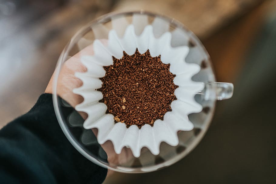 person holding clear glass mug, ground coffee on white strainer HD wallpaper