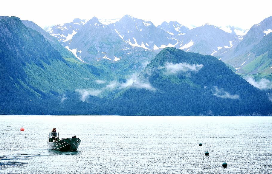 person riding on jon boat during daytime, boat on calm body of water next to mountains