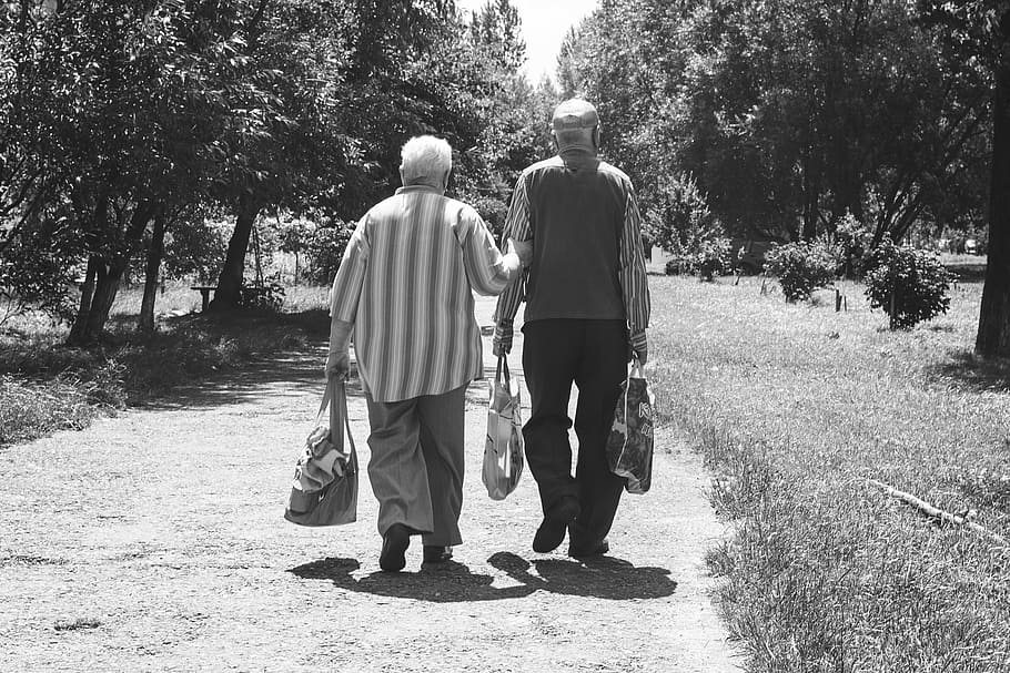 grayscale photo of man and woman walking on dirt road, old age