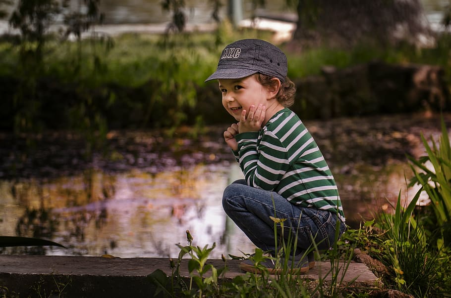 selective focus photo of a boy squatting near body of water HD wallpaper