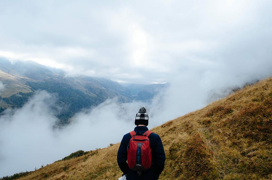 man with red backpack on top of foggy mountai n, man standing on hill HD wallpaper