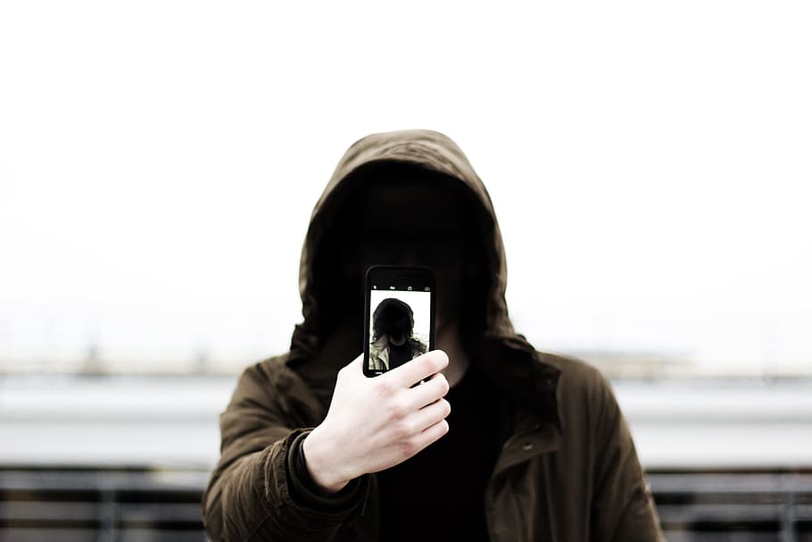 man wearing black hooded jacket and holding smartphone white taking close-up selfie, person in brown hoodie taking selfie outdoors