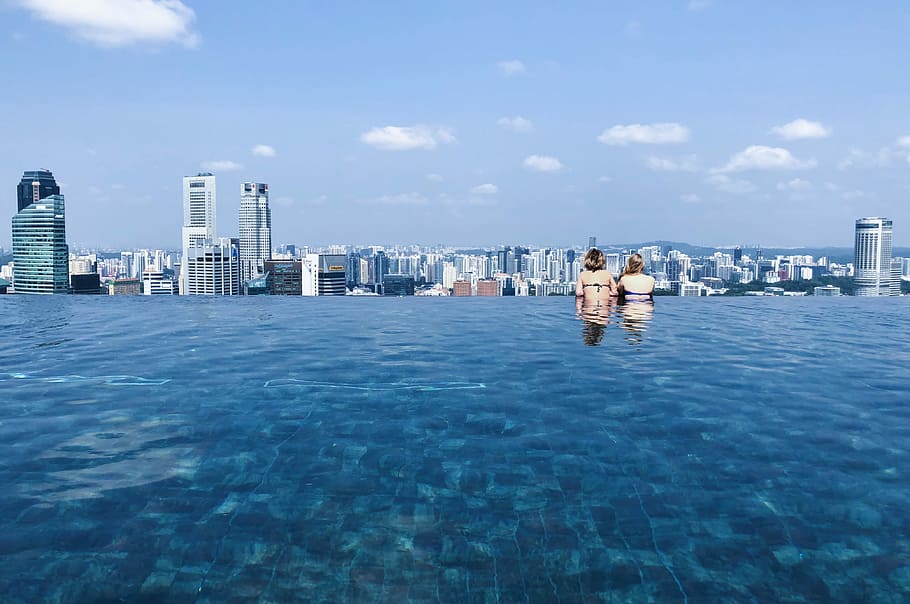 two women's swimming in pool while looking at building, two woman in swimming pool overlooking city view