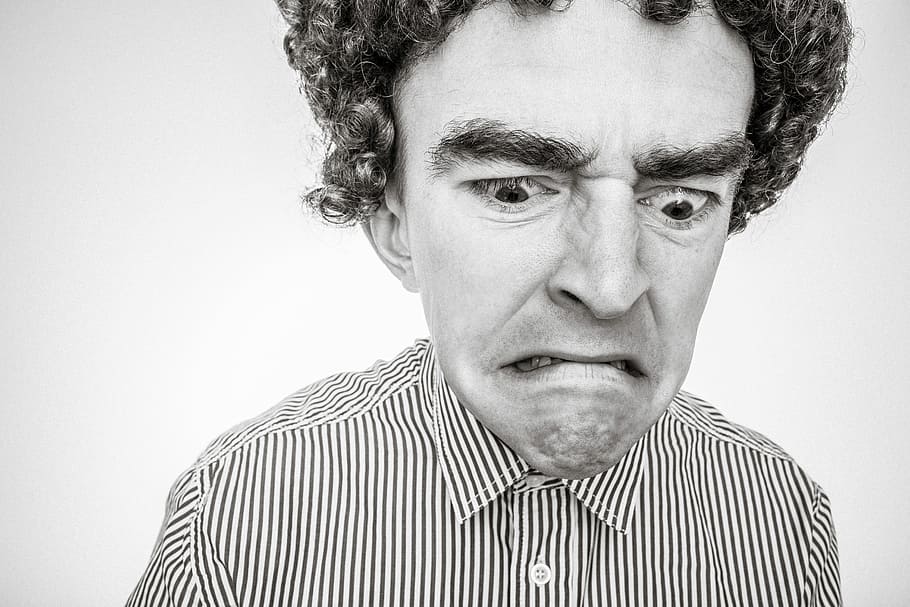 curly-haired man with and grumpy face wearing stripe collared shirt close-up and grayscale photo