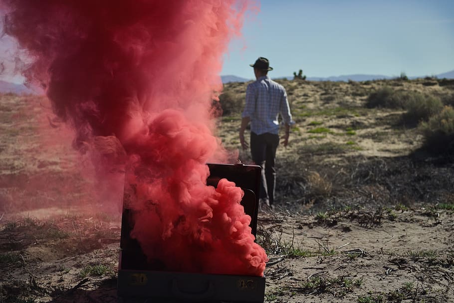 red smoke bomb on chest near man wearing black cap, person in white top and black hat walking in forest HD wallpaper