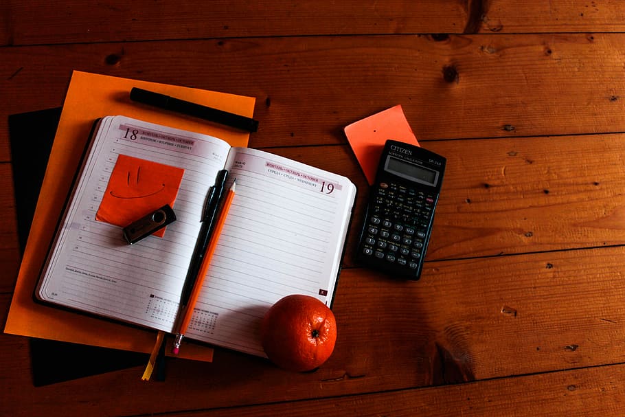 black scientific calculator, orange, and notebook on table, calculator near notebook on brown wooden surface HD wallpaper
