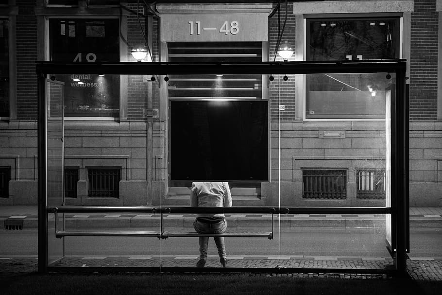 person sitting on bench beside glass building during nighttime HD wallpaper