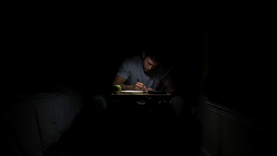 man writing in dark room, man writing on book inside room, desk