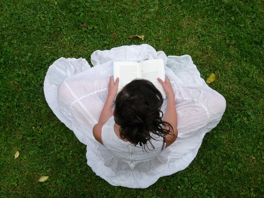 woman in white dress sitting on green grass while reading books during daytime HD wallpaper