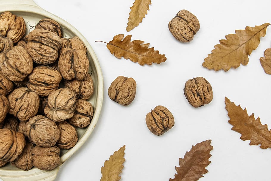 brown walnuts on beige ceramic bowl, flat-lay photography of nuts and leaves HD wallpaper