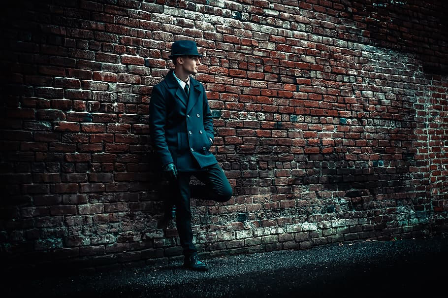 man wearing black coat leaning on brown brick wall, man leaning on wall HD wallpaper