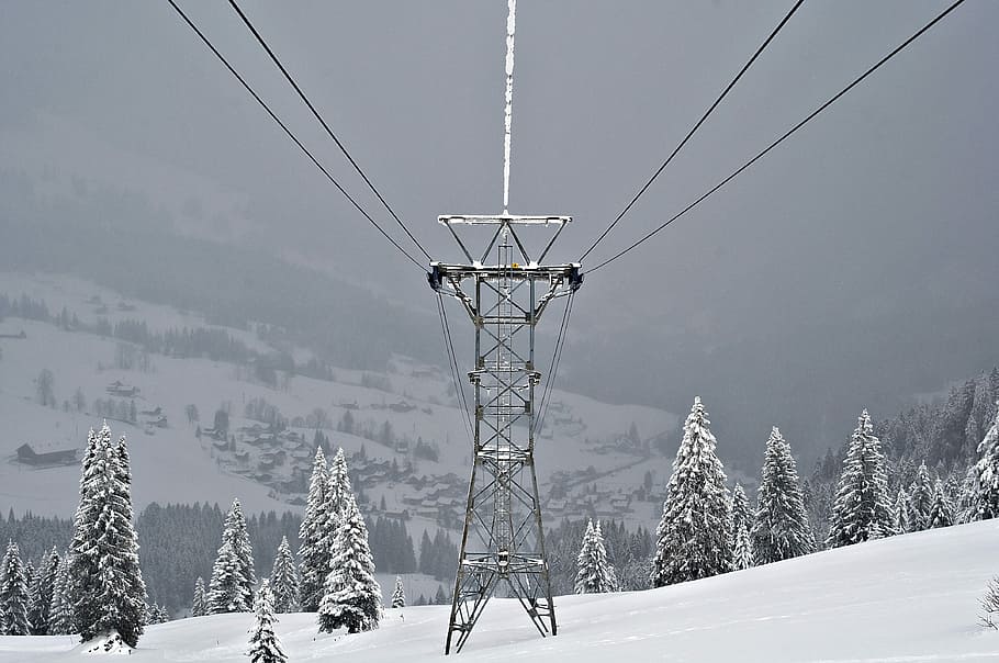 black metal transmission line covered with snow, grey transmission tower on snow mountains surrounded by pine trees HD wallpaper