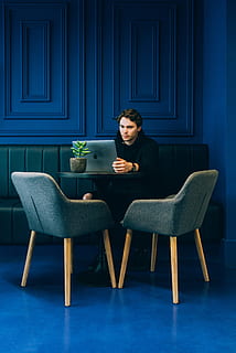 man sitting on couch with looking at his MacBook on table, man using MacBook while sitting on green sofa inside room HD wallpaper