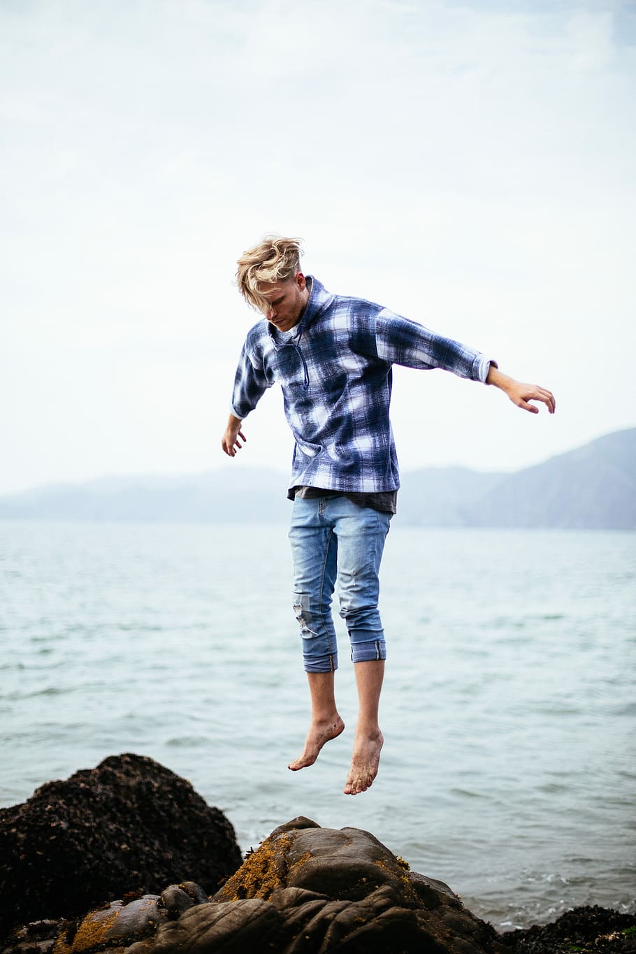 man jumping on rock near body of water, person on mid air below brown rock beside body of water during daytime HD wallpaper