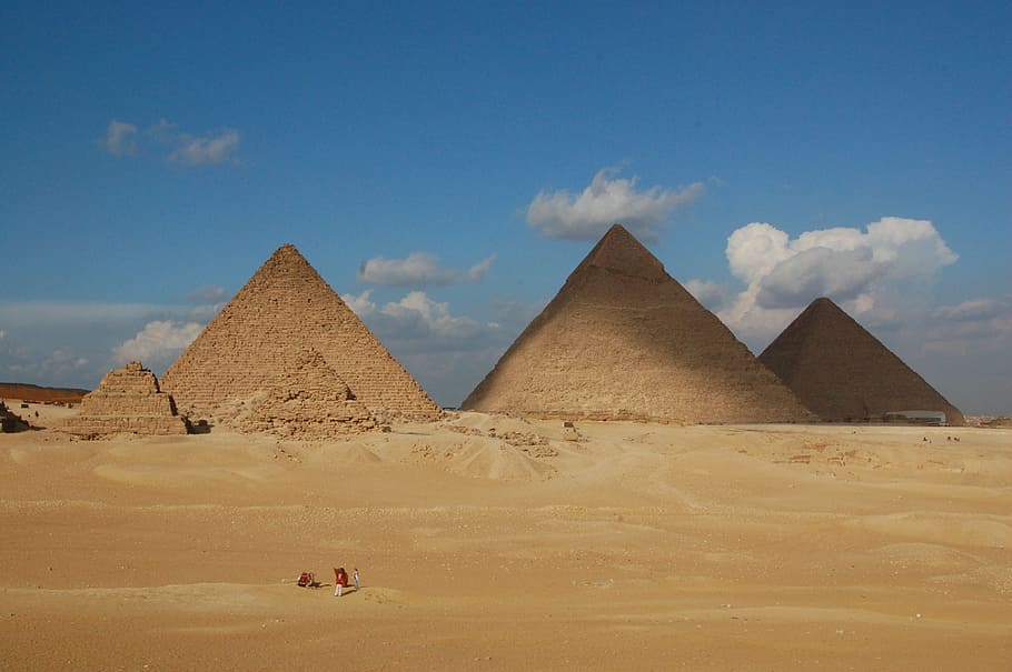 two peoples stands on dessert near pyramid at daytime, pyramids