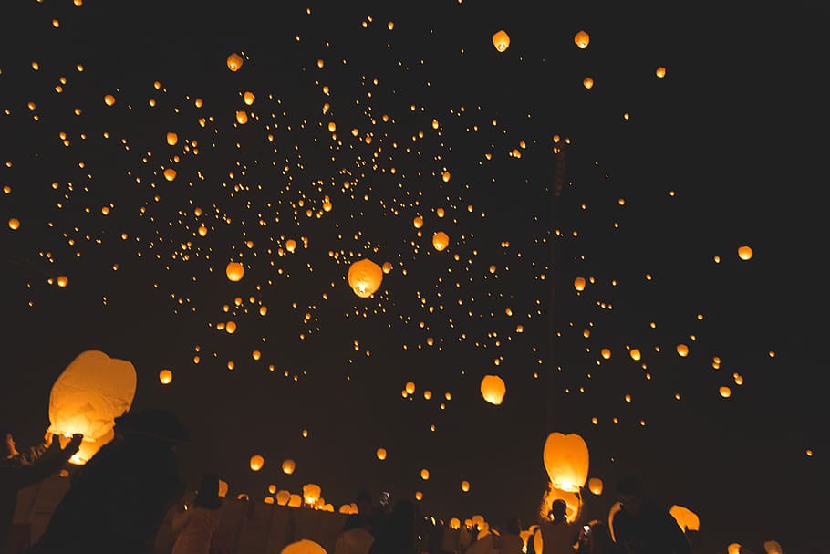 people raising sky lanterns, sky lanterns floating on air at nighttime
