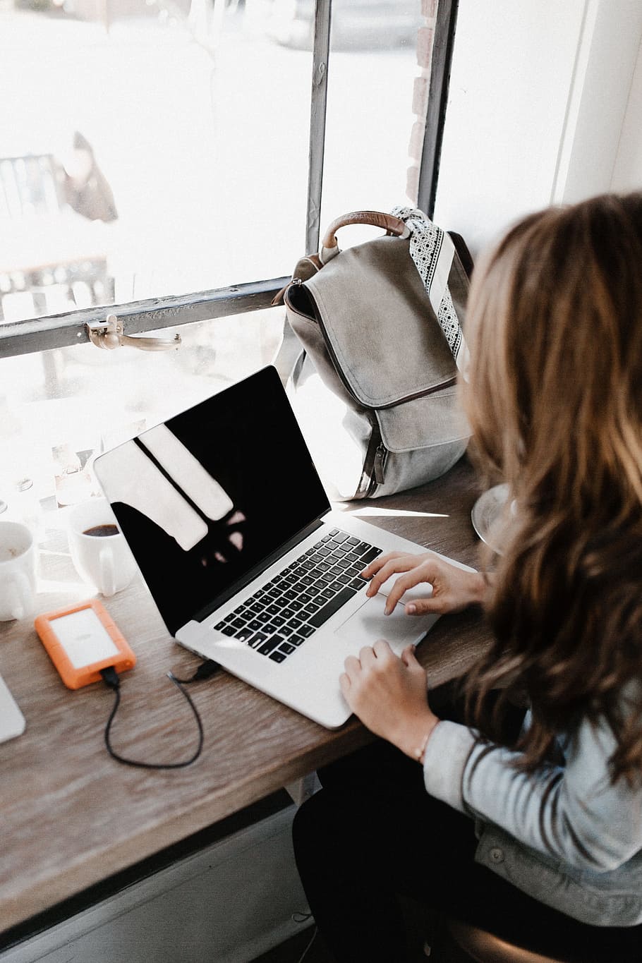 girl wearing grey long-sleeved shirt using MacBook Pro on brown wooden table, person typing on MacBook Pro HD wallpaper