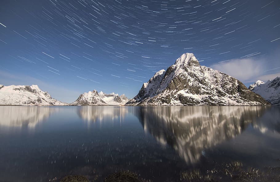 timelapse photography of mountain alps near water with stars, landscape photography of body of water and gray rock mountains covered with snow at daytime HD wallpaper