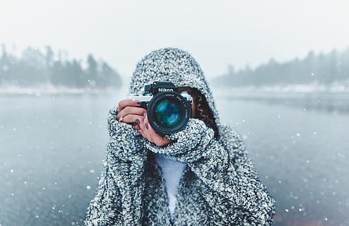 selective focus photo of a person holding black Nikon DSLR camera about to take a picture during snow season HD wallpaper