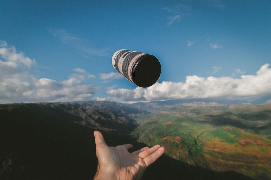person throwing black and white Canon lens, person throwing black and gray container under blue sky HD wallpaper