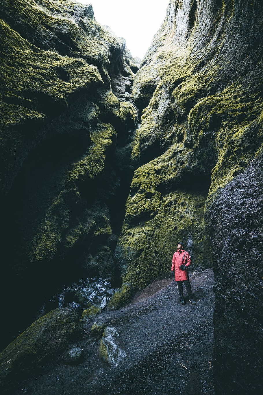 person standing between of hollow cliff, man wearing red coat near stones HD wallpaper
